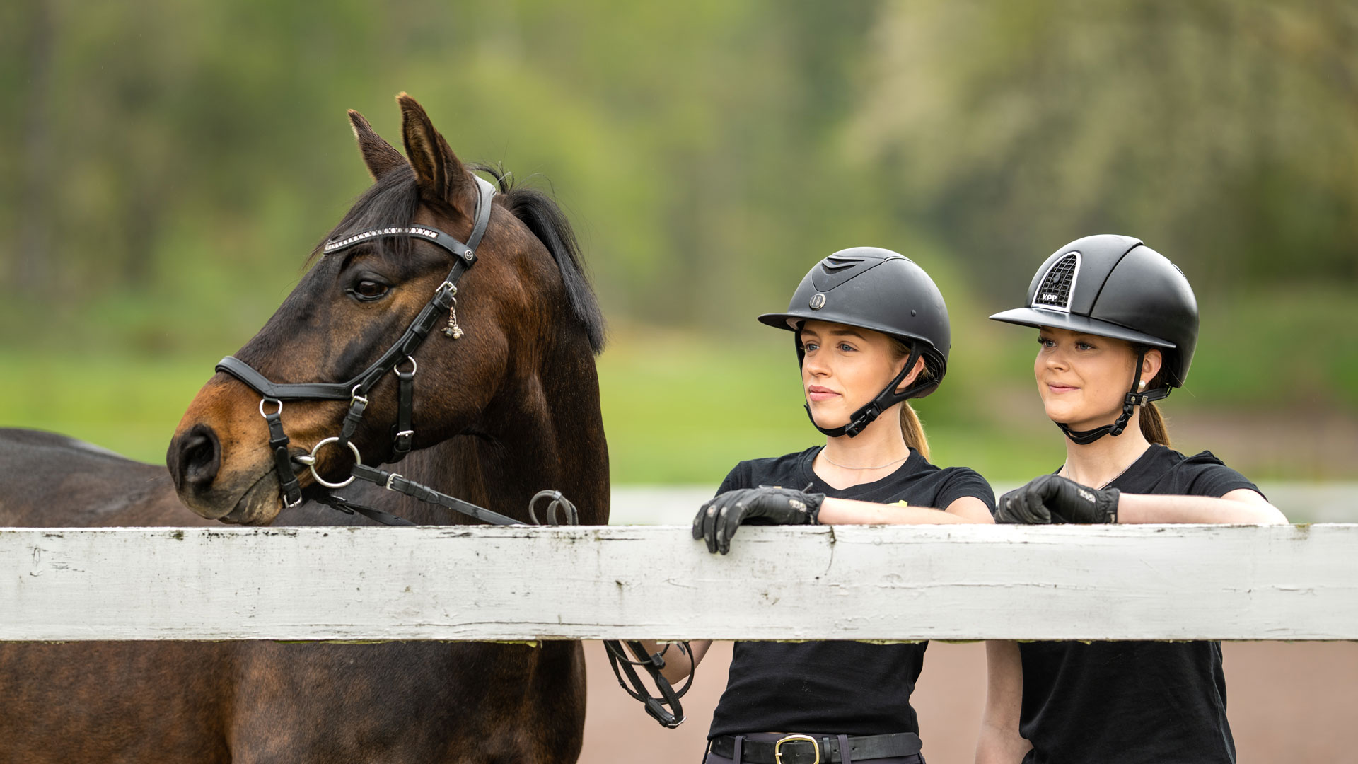 två tjejer och en häst vid staket