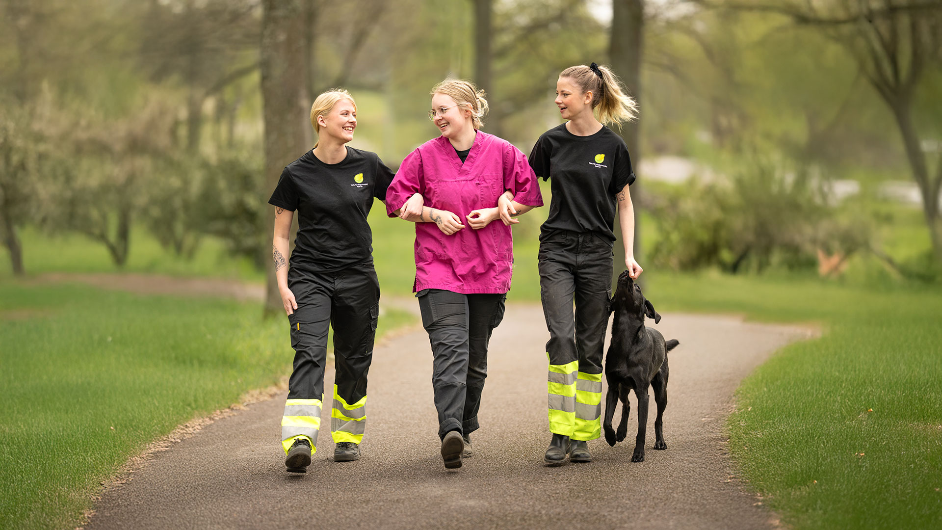 tre elever som håller om varandra och går tillsammans med en hund